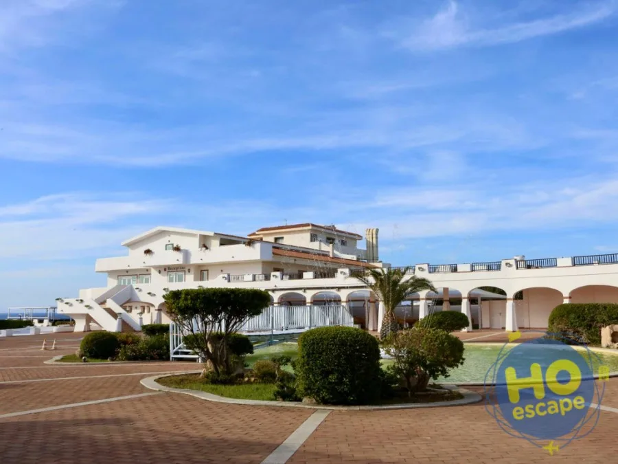 Esterno dell'hotel bianco con reception, portici e giardino curato