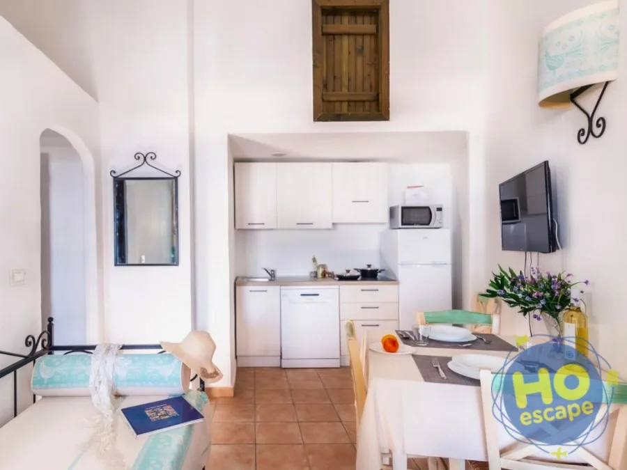 Soggiorno luminoso con angolo cottura attrezzato, zona pranzo apparecchiata e divanetto con cuscini decorati