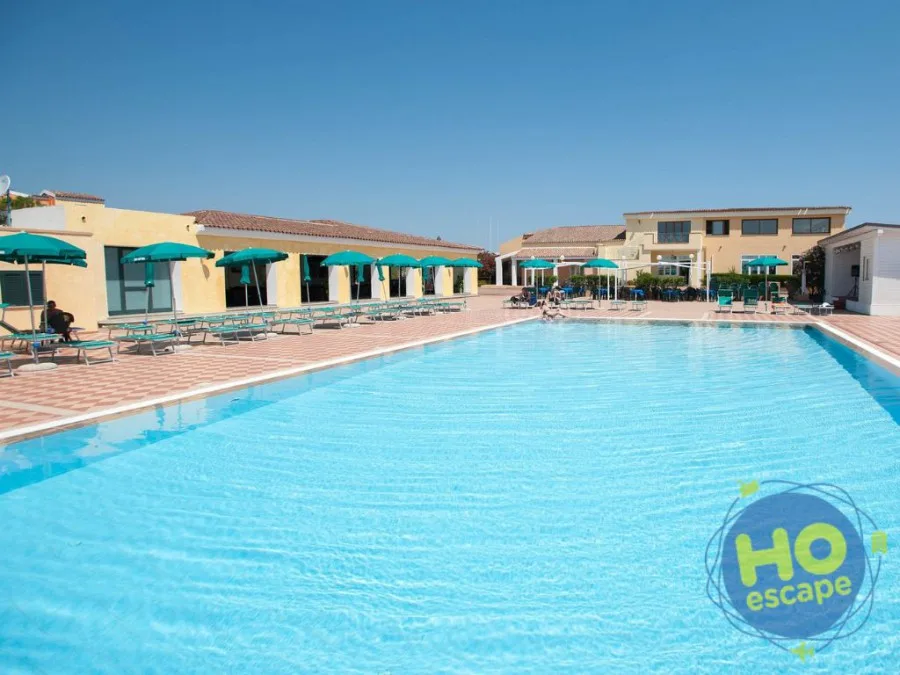 Grande piscina con lettini e ombrelloni verdi accanto agli edifici gialli del resort