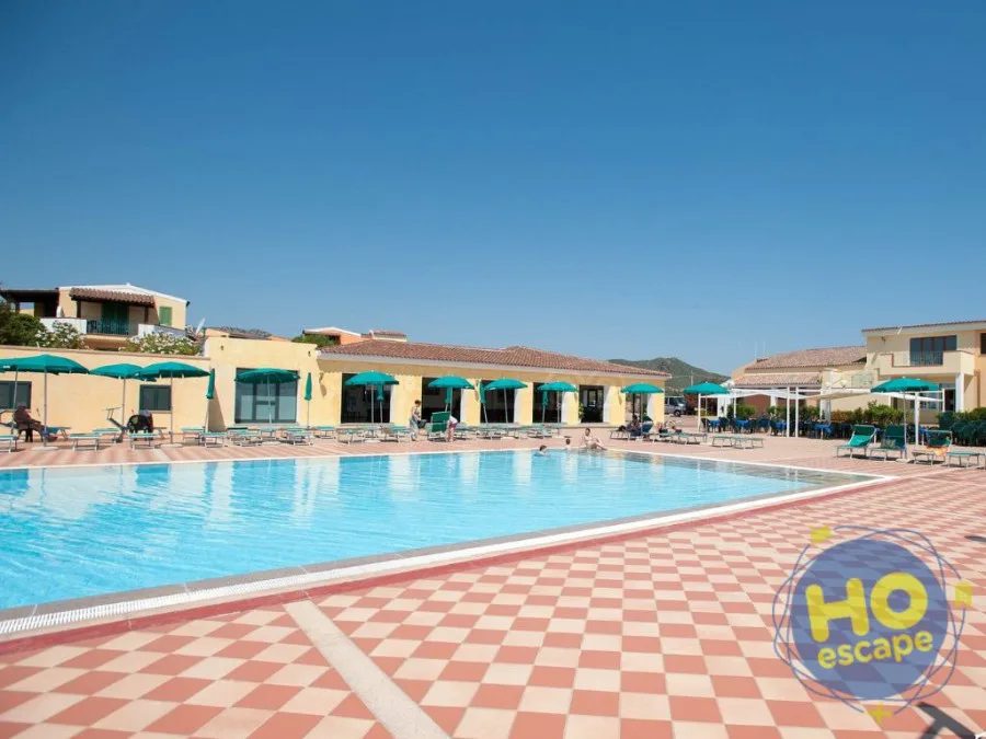 Piscina rettangolare con bordo a scacchi, ombrelloni verdi e edifici del resort sullo sfondo