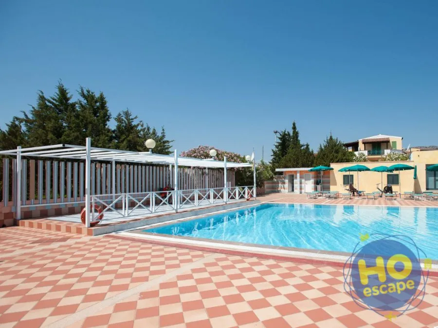 Piscina con pergolato bianco, ombrelloni verdi e alberi sotto un cielo limpido