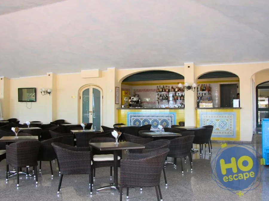 Bar interno dell'hotel con tavoli in rattan, decorazioni in maiolica e bancone fornito