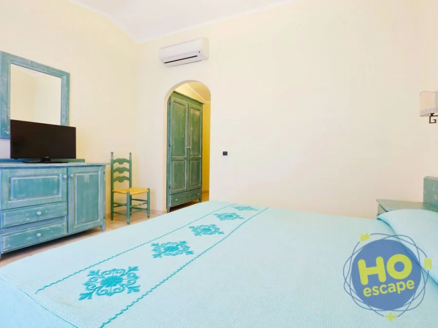 Camera con letto, cassettiera in legno azzurro, specchio e armadio in stile sardo