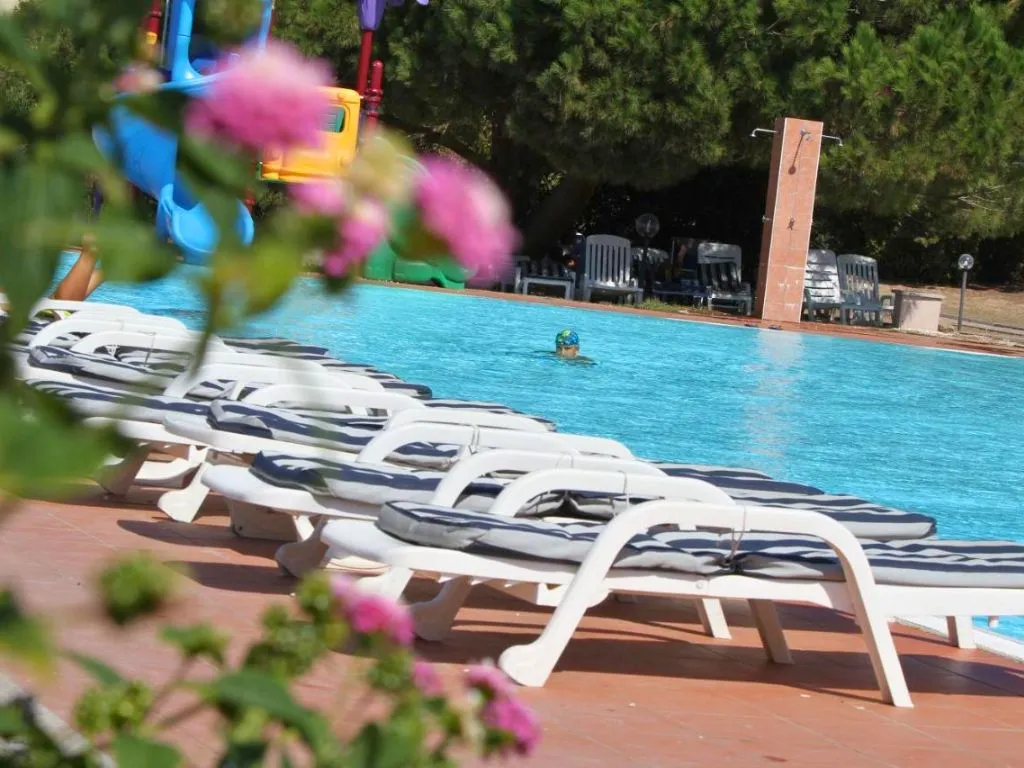 Lettini bianchi a bordo piscina con fiori in primo piano e bambino in acqua