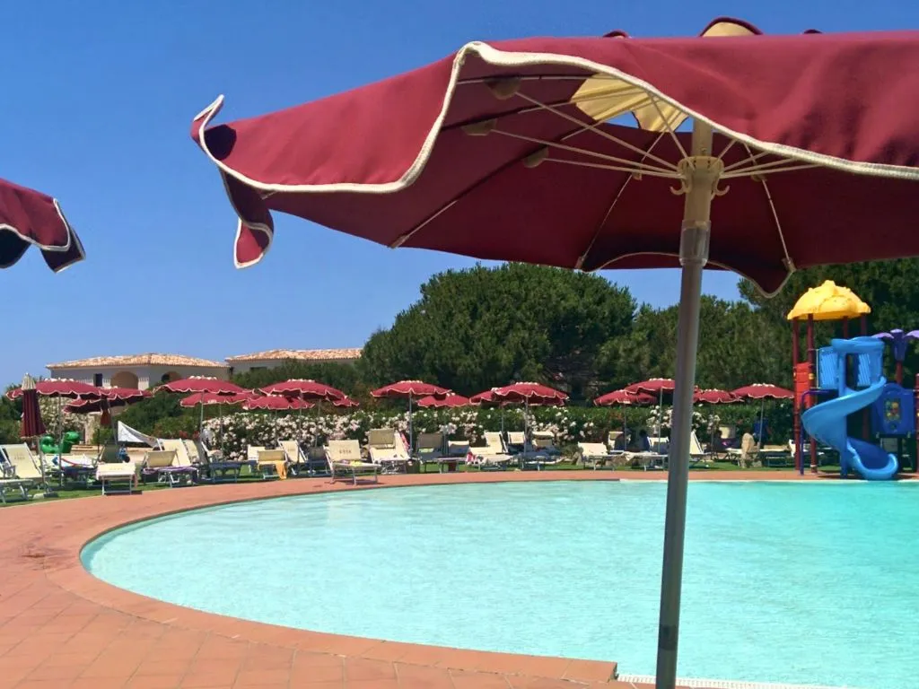 Piscina con ombrellone rosso, lettini e area giochi acquatici