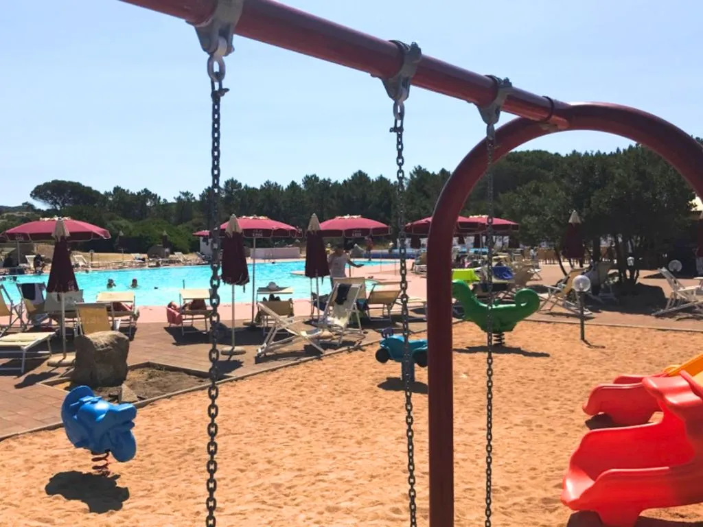 Area giochi per bambini con altalene accanto alla piscina