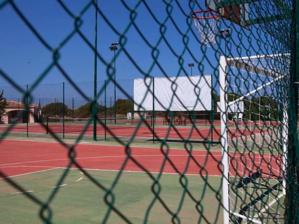 Campi sportivi con canestro da basket e campo da tennis visti attraverso la rete
