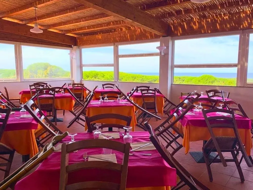 Sala ristorante con tovaglie colorate e ampie vetrate con vista sul verde e mare