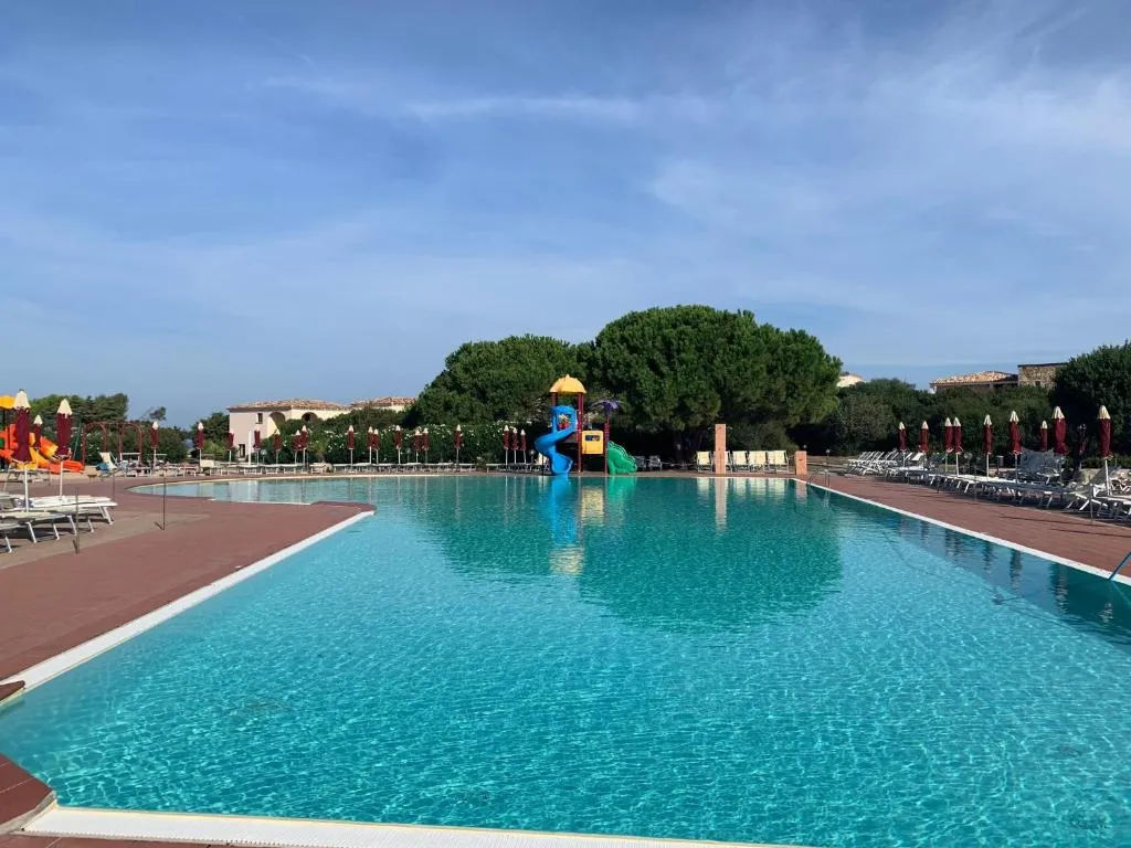 Grande piscina con scivoli colorati e lettini circondata da pini