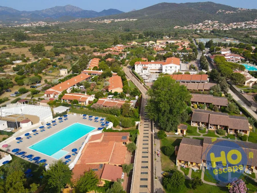 Veduta aerea del resort con piscina, ville dai tetti rossi e colline sullo sfondo
