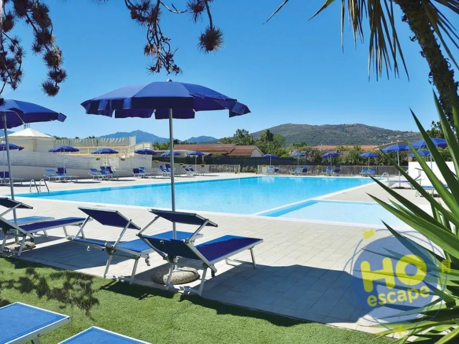 Piscina con lettini e ombrelloni blu, prato verde e montagne sullo sfondo