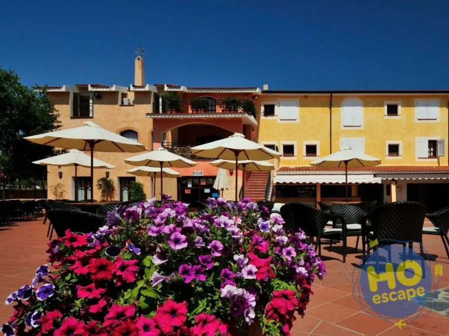 Esterno del resort con edifici colorati, terrazza con tavoli e fiori in primo piano