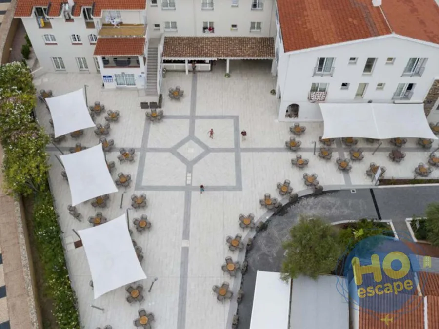 Vista aerea del cortile centrale dell'hotel con tavoli rotondi, teli ombreggianti e pavimentazione decorata