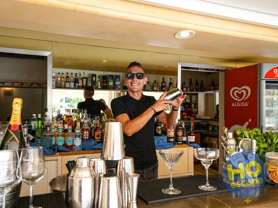 Barman sorridente prepara cocktail con shaker dietro al bancone ben fornito
