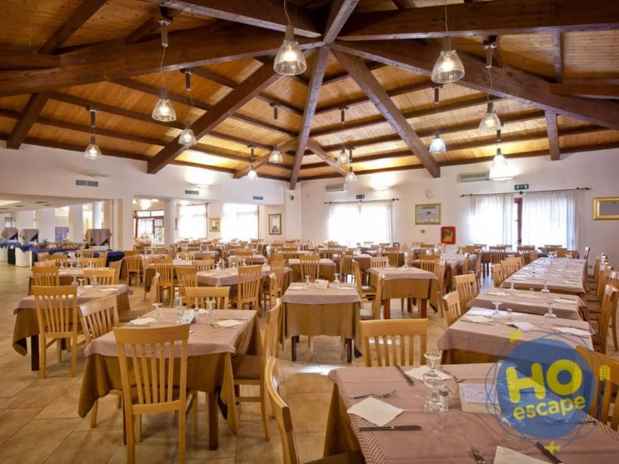Ampia sala ristorante interna con soffitto in legno a travi, tavoli apparecchiati e sedie in legno