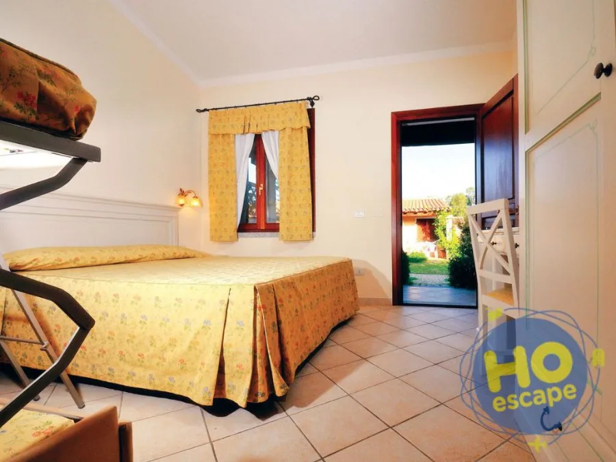 Camera da letto luminosa con letto matrimoniale dalla coperta gialla a fiori, letto a castello e porta che si apre sul giardino esterno
