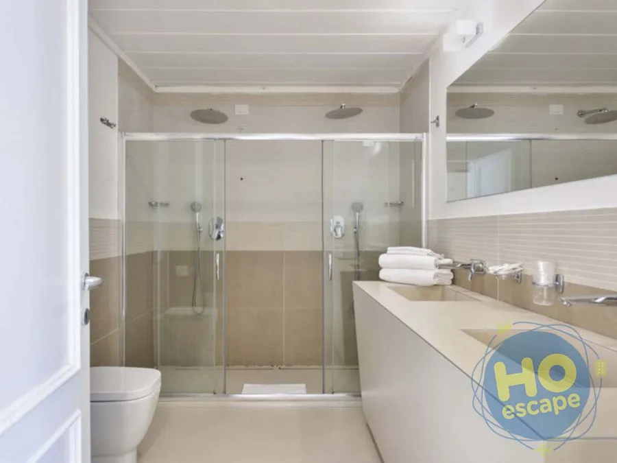 Bagno moderno con ampia doccia in vetro, soffione a pioggia, doppio lavabo e WC su toni beige e crema
