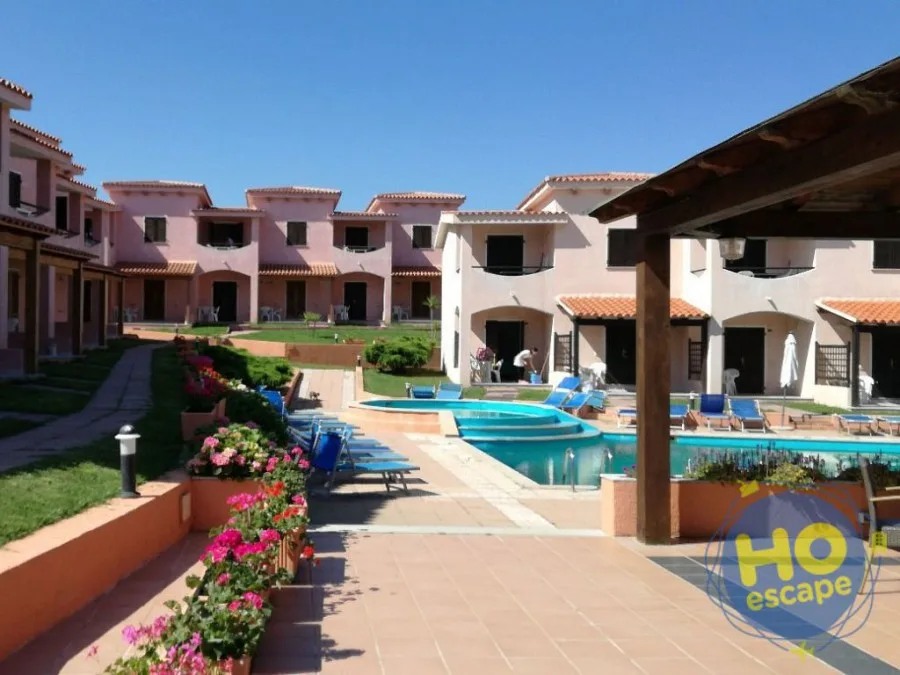 Cortile del residence con piscina, lettini e villette rosa con fiori colorati