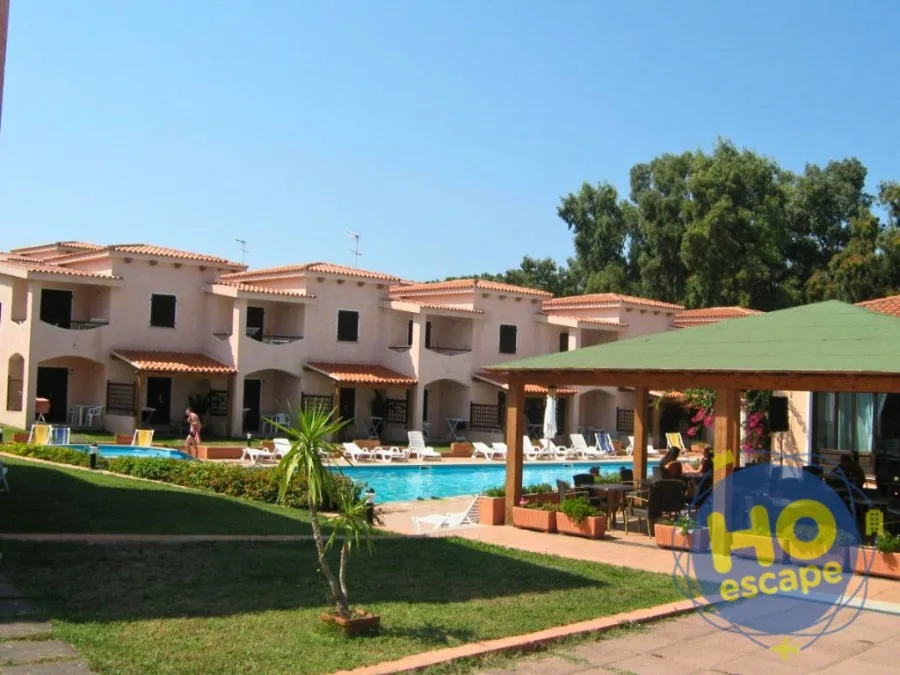Piscina del villaggio con villette beige e gazebo in legno con tetto verde