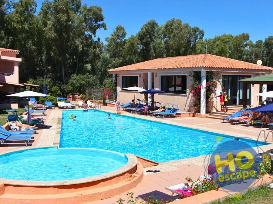 Piscina con vasca idromassaggio circolare, lettini blu ed edificio con tetto in coppi