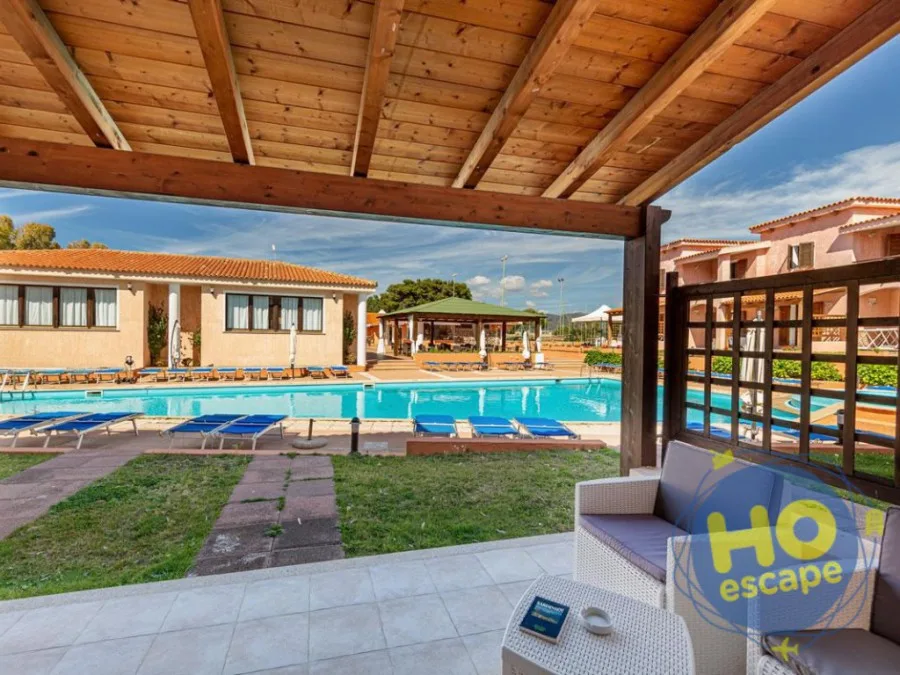 Veranda in legno con divano in rattan vista piscina e lettini blu