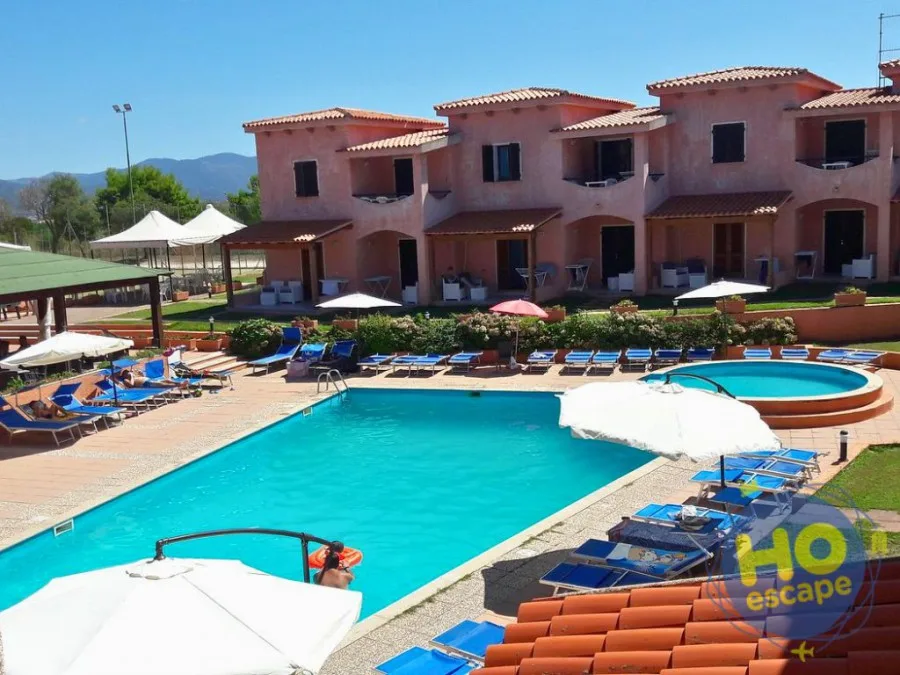 Piscina con vista sulle villette rosa, lettini blu e montagne sullo sfondo