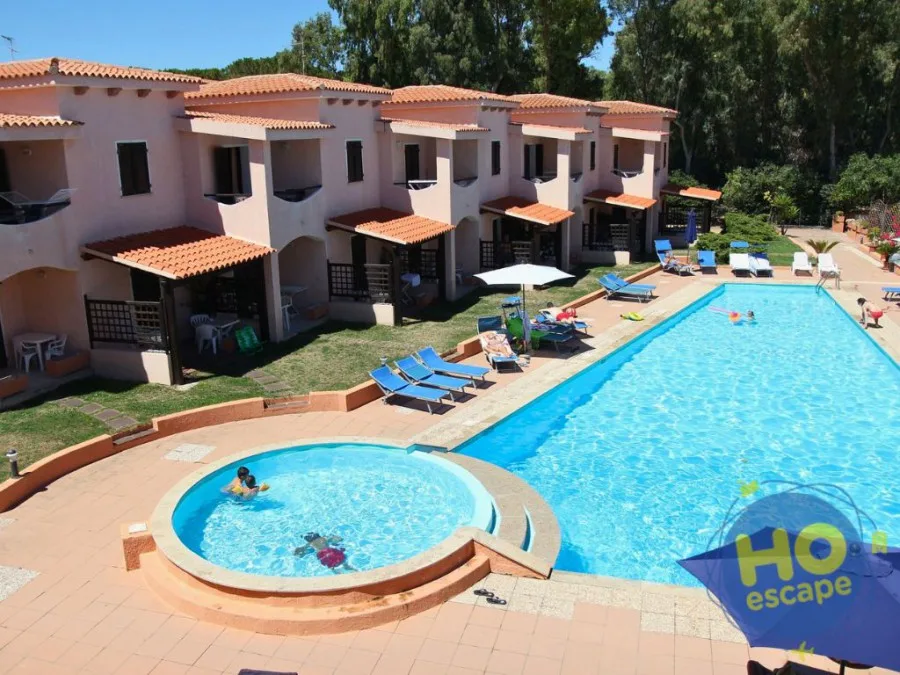 Piscina con villette rosa, ombrelloni e lettini blu circondata dal verde