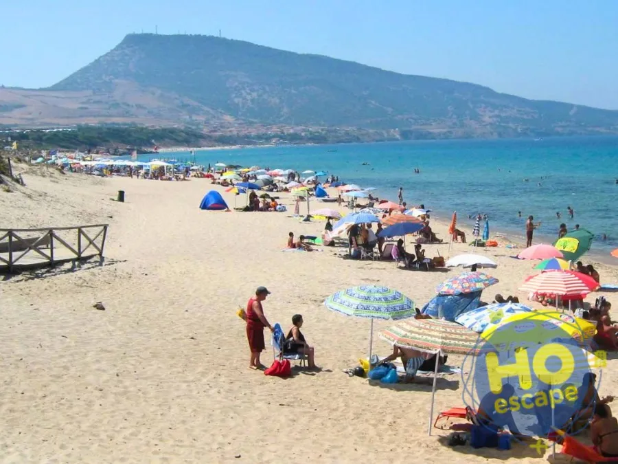 Spiaggia affollata con ombrelloni colorati e collina sullo sfondo