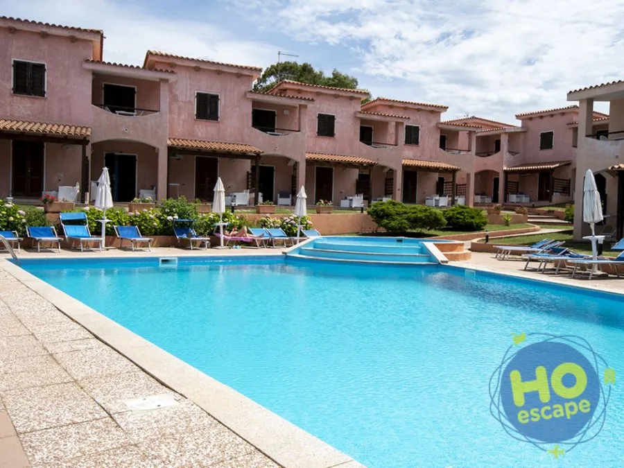 Piscina del residence con villette rosa, lettini blu e ombrelloni
