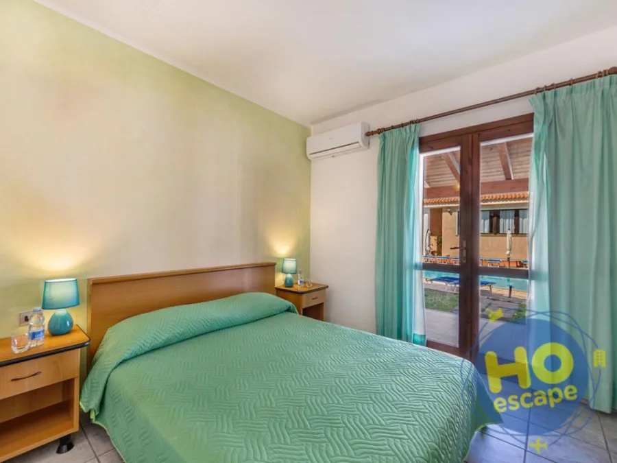 Camera da letto con copriletto verde e porta finestra sulla piscina
