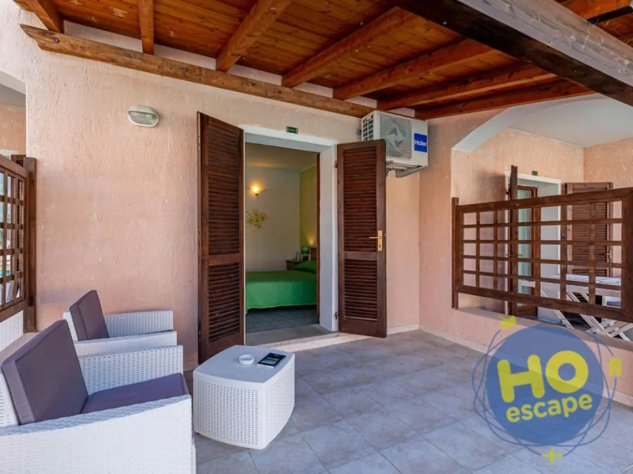 Patio esterno con divani in rattan e accesso alla camera con letto verde