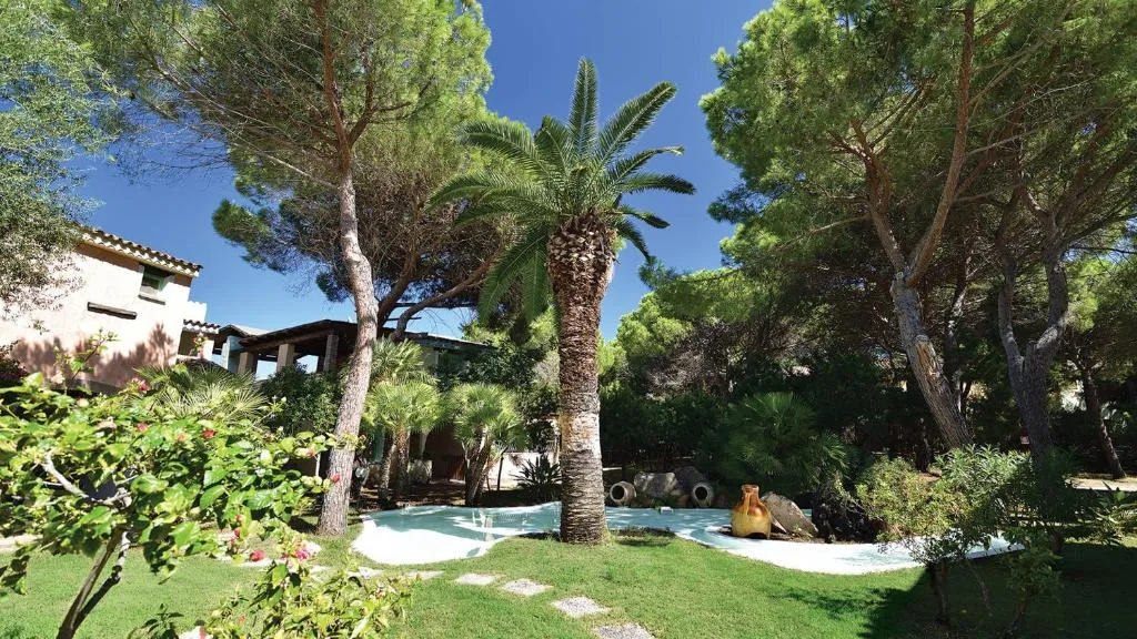 Giardino rigoglioso con palme, pini e vegetazione tra le strutture del resort