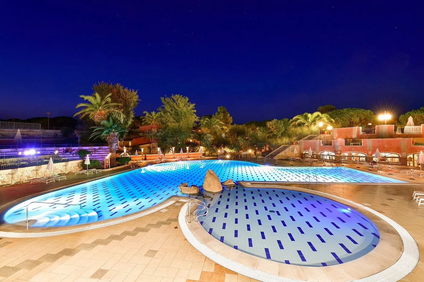 Piscina illuminata di sera con palme e atmosfera notturna