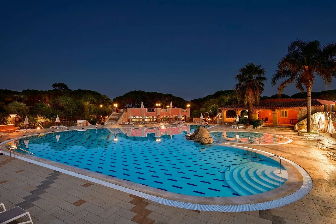 Piscina al crepuscolo con riflessi e edifici illuminati del resort