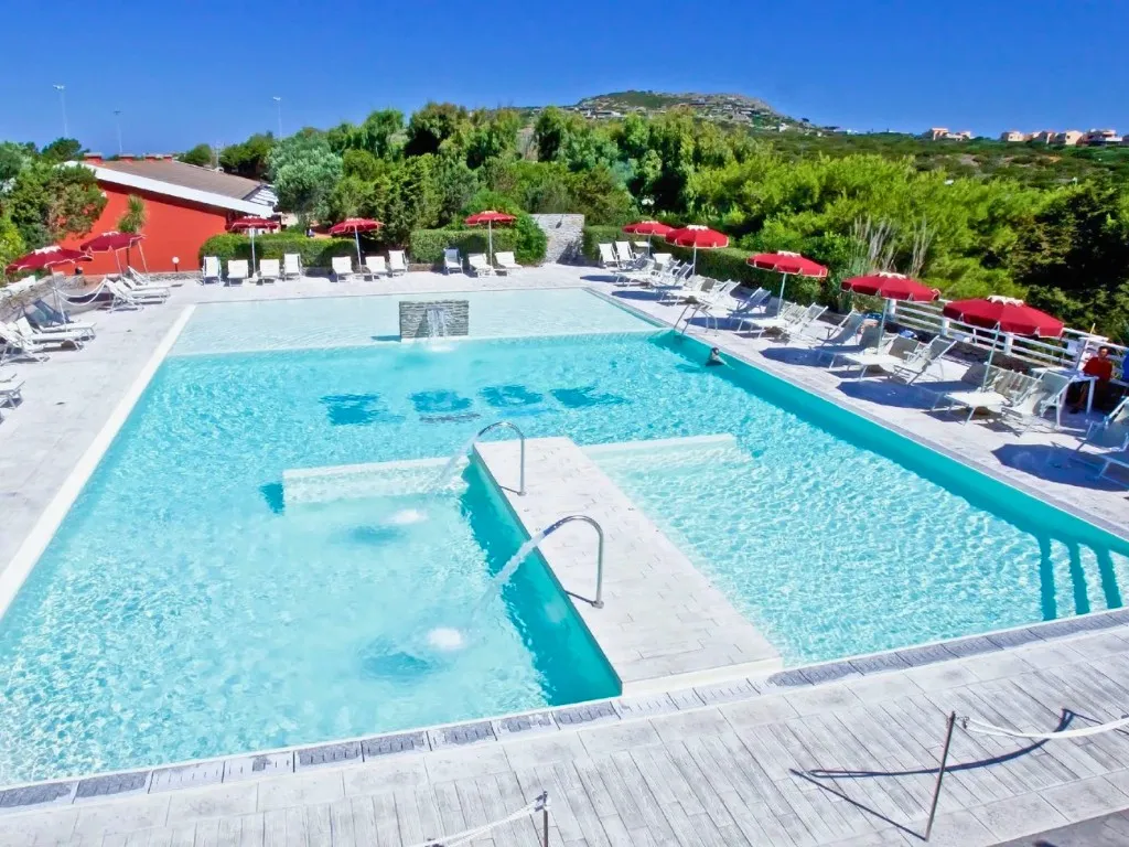 Piscina con cascate d'acqua e ombrelloni rossi immersa nella vegetazione