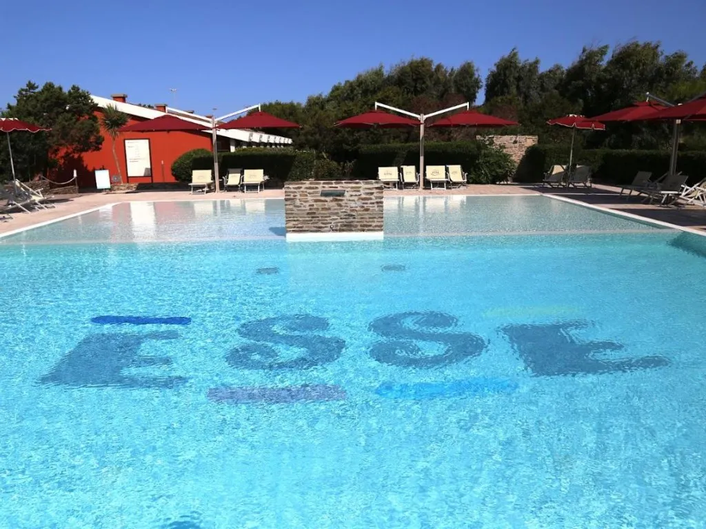 Piscina con scritta ESSE sul fondo e ombrelloni rossi del Club Esse