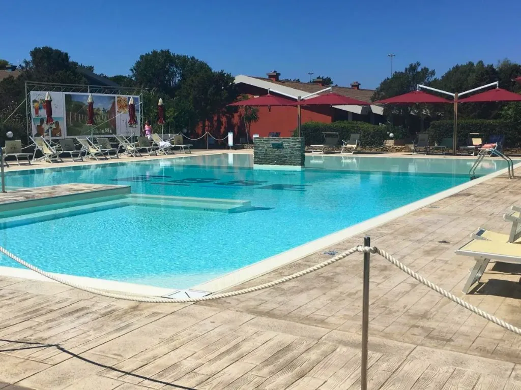 Piscina con ombrelloni rossi e lettini accanto agli edifici del resort
