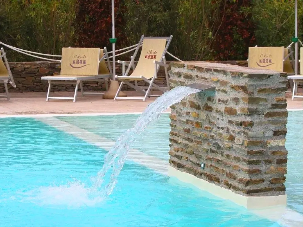 Dettaglio di cascata d'acqua in pietra in piscina con lettini Club Esse