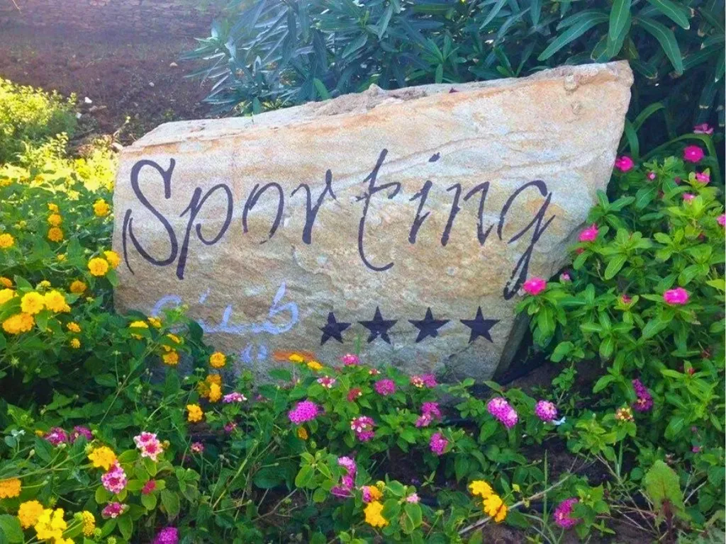Insegna in pietra Sporting Club a quattro stelle tra fiori colorati