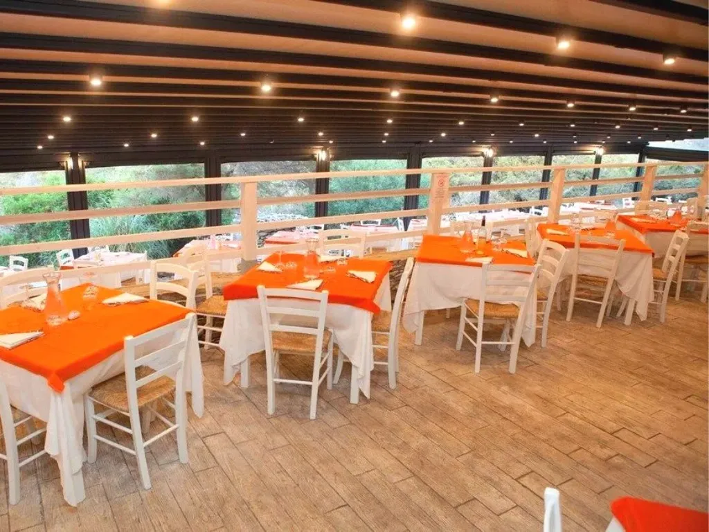 Sala interna del ristorante con tavoli arancioni e ampie vetrate sul verde