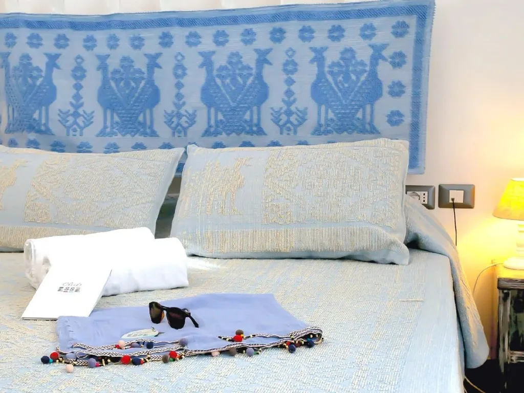 Dettaglio del letto con testiera decorata in stile sardo e accessori da spiaggia