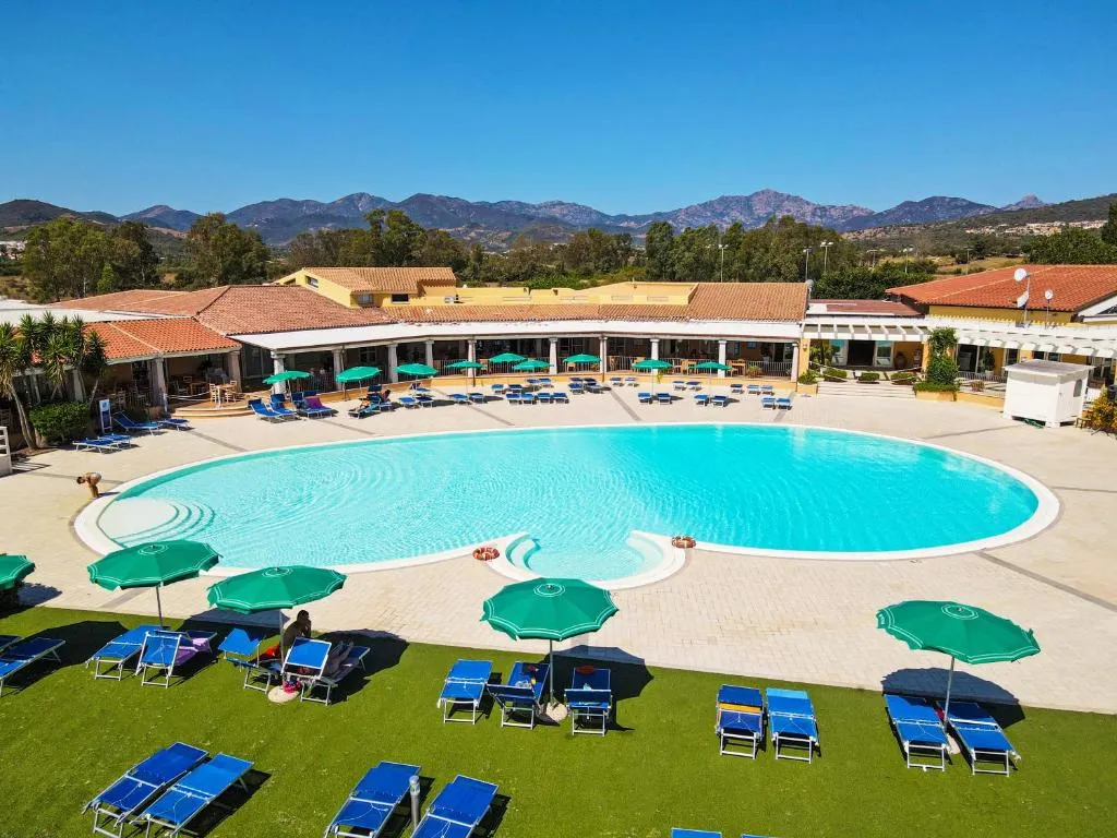 Piscina rotonda con ombrelloni verdi, lettini blu e colline sullo sfondo