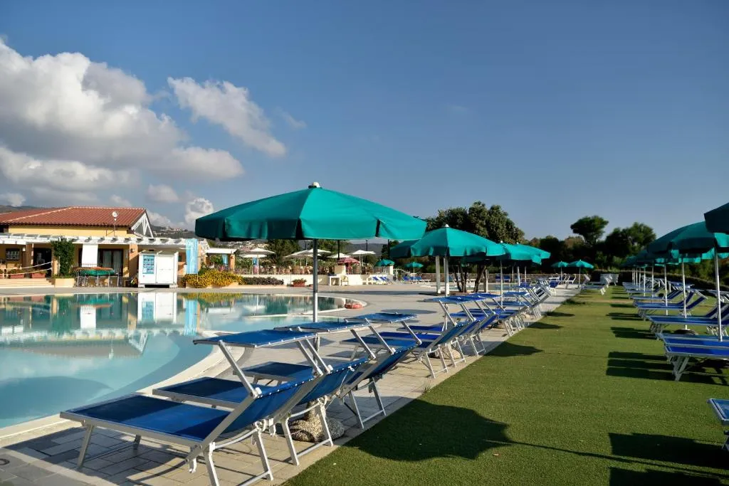 Bordo piscina con file di lettini blu e ombrelloni verdi su prato verde