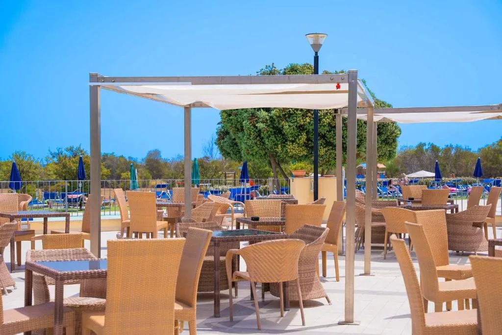 Terrazza esterna con tavoli, sedie in rattan e gazebo bianco vicino alla piscina