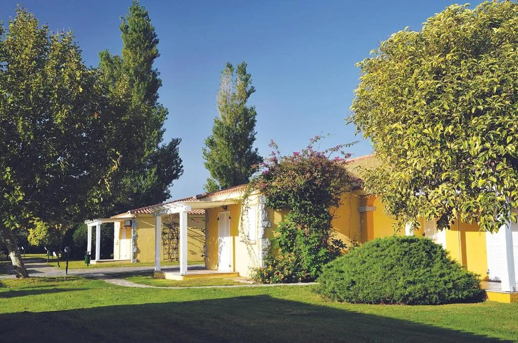 Casetta gialla del villaggio immersa nel verde con alberi e fiori