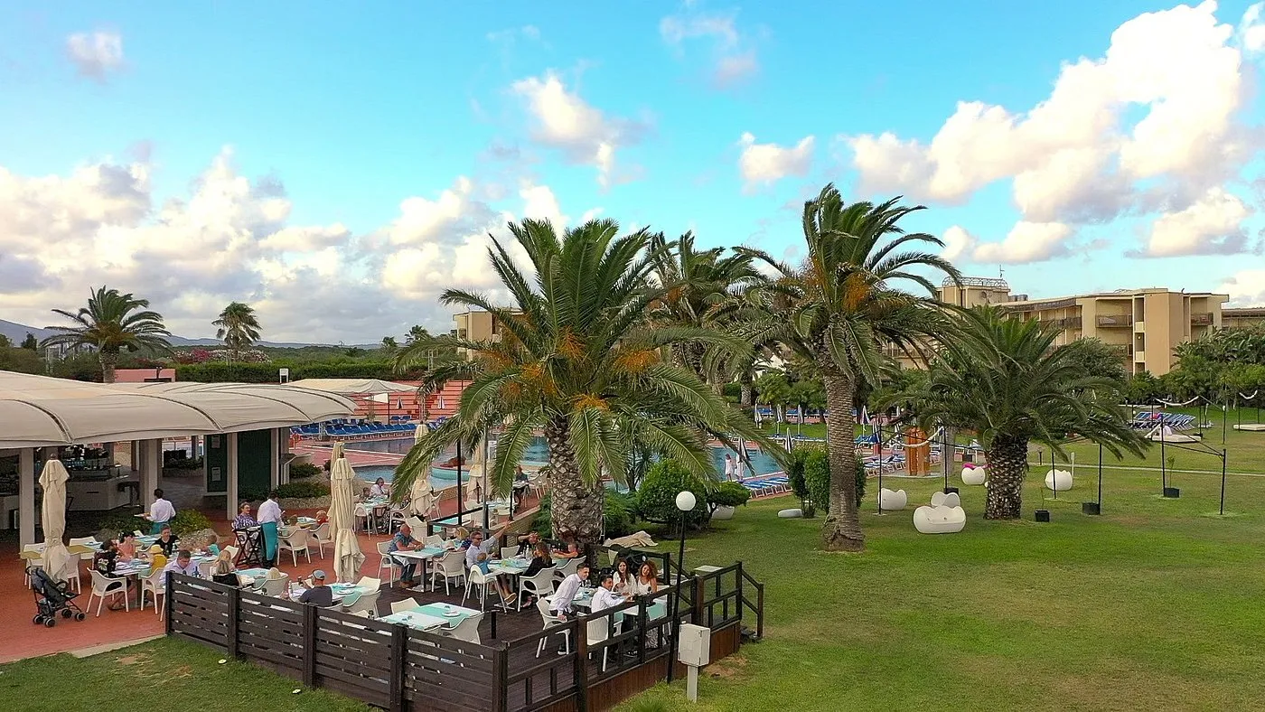 Terrazza ristorante all'aperto con tavoli, palme e vista sulla piscina