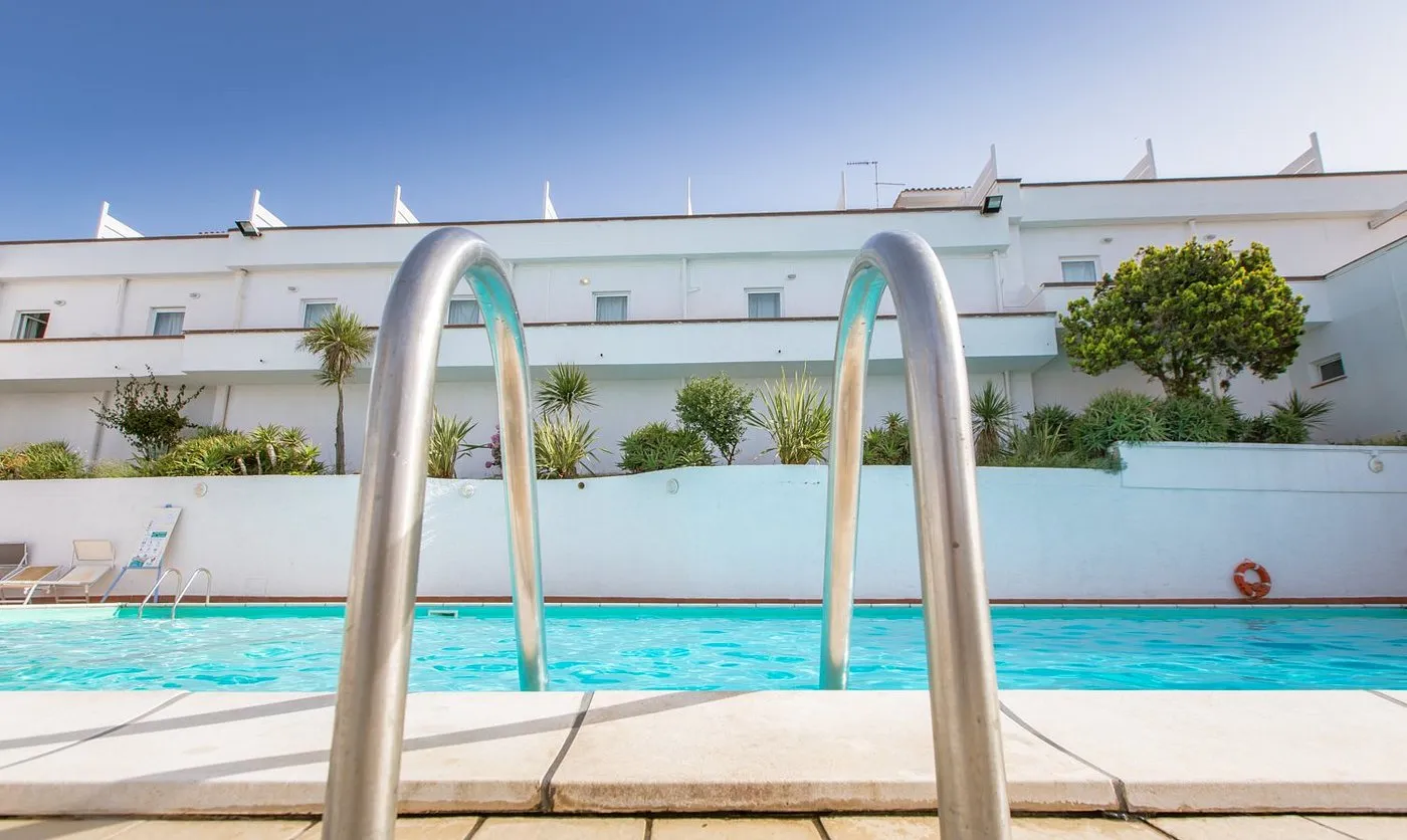 Dettaglio della scaletta di una piscina con edificio bianco dell'hotel alle spalle