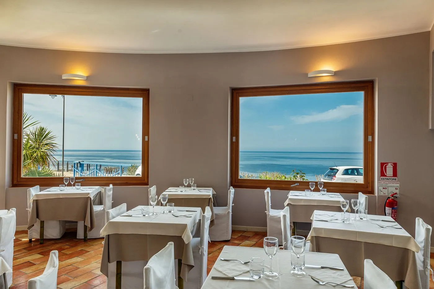 Sala da pranzo con tavoli apparecchiati e ampie finestre con vista sul mare