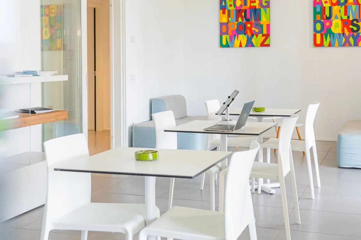 Sala comune luminosa con tavoli bianchi e quadri colorati