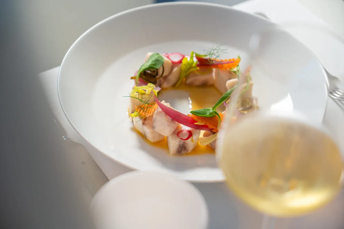 Piatto gourmet di pesce impiattato con verdure e vino bianco